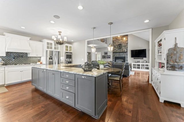 kitchen with gray cabinets, a stone fireplace, white cabinets, a notable chandelier, and stainless steel appliances