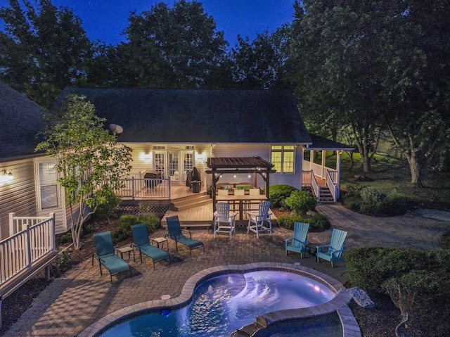 pool at twilight with french doors, a pool with connected hot tub, a wooden deck, and a patio area