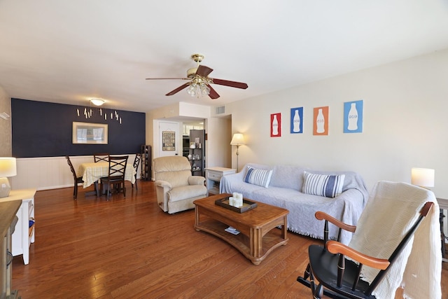 living area with visible vents, a ceiling fan, wood finished floors, and a wainscoted wall
