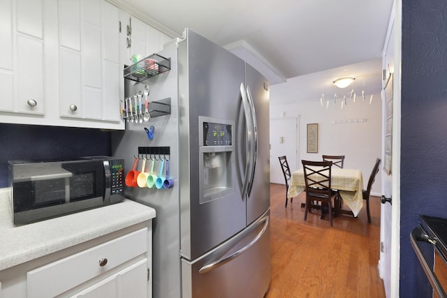 kitchen featuring black microwave, stainless steel refrigerator with ice dispenser, light countertops, white cabinetry, and light wood-type flooring