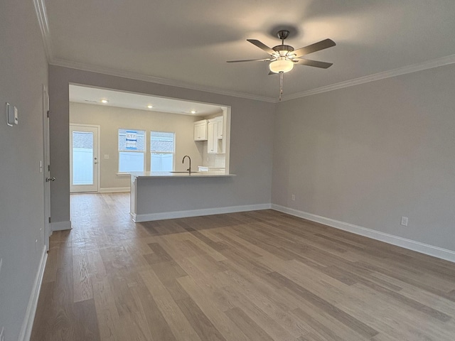 unfurnished living room featuring baseboards, a sink, ceiling fan, and wood finished floors