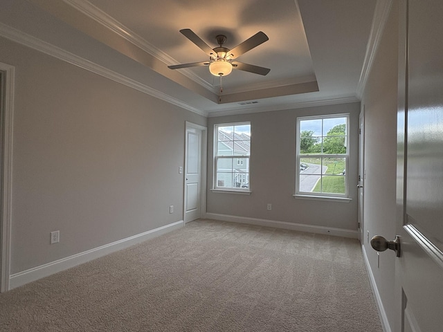 empty room with a tray ceiling, light colored carpet, and ornamental molding