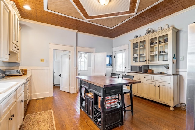 kitchen featuring crown molding, stainless steel microwave, cream cabinets, and a wainscoted wall
