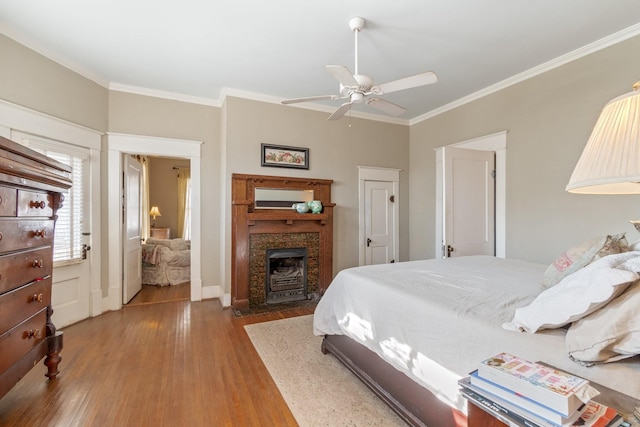 bedroom with ornamental molding, a fireplace with flush hearth, ceiling fan, and wood finished floors
