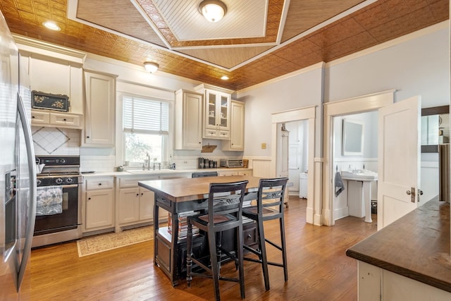 kitchen with a sink, wood finished floors, gas range, ornamental molding, and glass insert cabinets