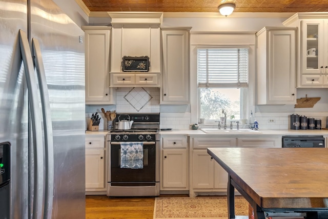 kitchen featuring gas range, crown molding, light countertops, a sink, and stainless steel fridge