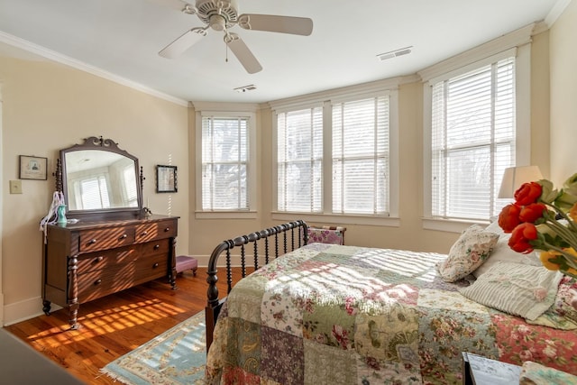 bedroom with crown molding, baseboards, wood finished floors, and visible vents
