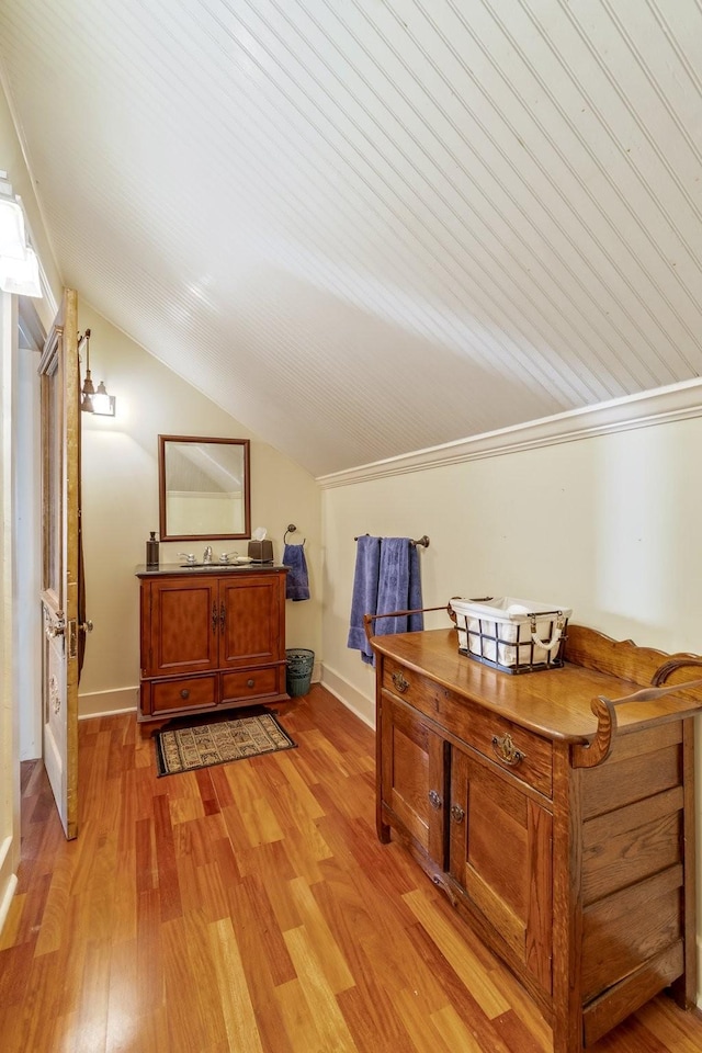 interior space with baseboards, light wood finished floors, and vaulted ceiling