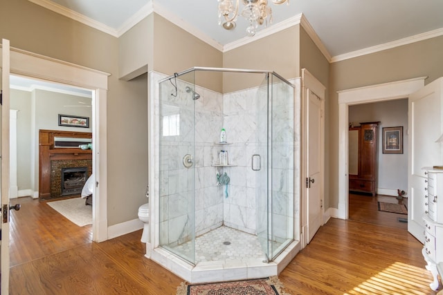 bathroom with a notable chandelier, a fireplace, toilet, a shower stall, and wood finished floors