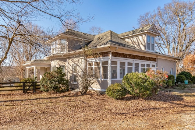 rear view of property featuring a sunroom, a shingled roof, and fence