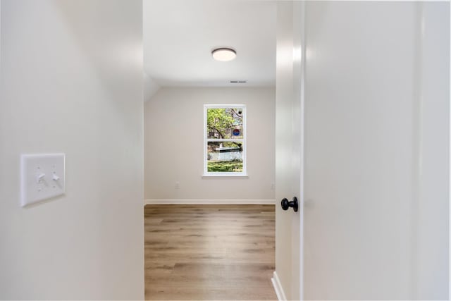 corridor featuring light wood-type flooring, baseboards, visible vents, and vaulted ceiling