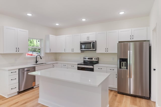 kitchen with white cabinets, stainless steel appliances, a sink, and light wood-style flooring