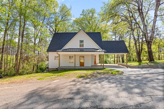 modern farmhouse style home with roof with shingles, a standing seam roof, covered porch, driveway, and metal roof