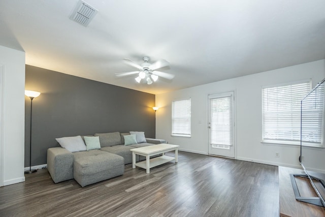 living room featuring visible vents, a ceiling fan, baseboards, and dark wood-type flooring