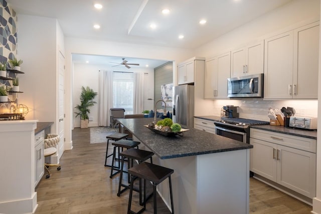 kitchen with light wood finished floors, an island with sink, stainless steel appliances, decorative backsplash, and a kitchen bar