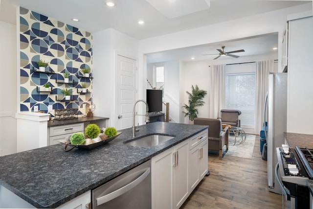 kitchen with wood finished floors, dark stone counters, white cabinets, a sink, and stainless steel appliances