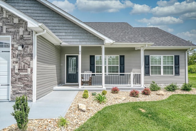 property entrance featuring a porch, a shingled roof, a lawn, and a garage