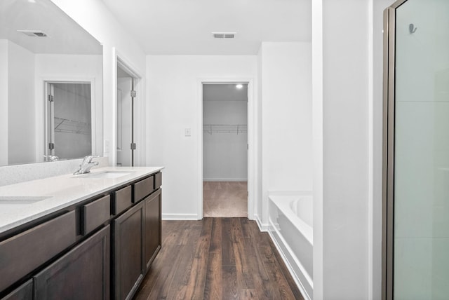 full bath featuring wood finished floors, a walk in closet, a bath, and double vanity