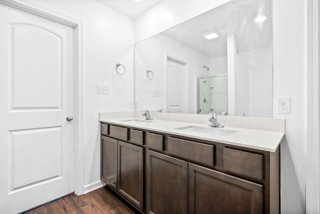 full bath featuring a stall shower, wood finished floors, double vanity, and baseboards