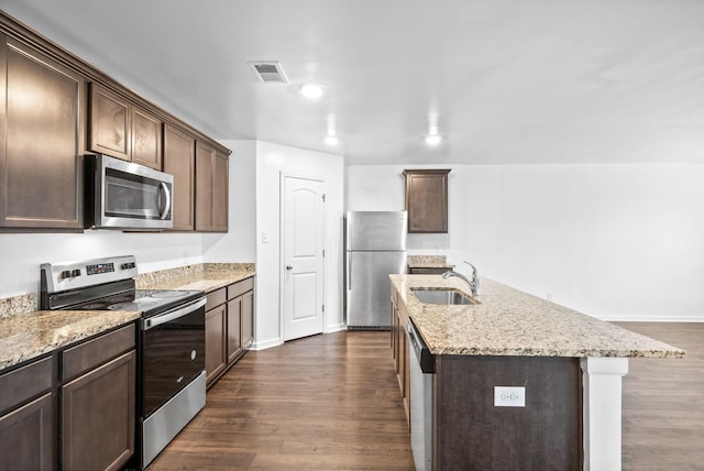 kitchen with appliances with stainless steel finishes, a sink, dark brown cabinets, light stone counters, and dark wood-style flooring