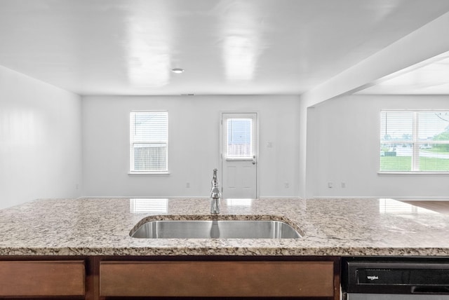 kitchen with dishwashing machine, a sink, light stone counters, and open floor plan