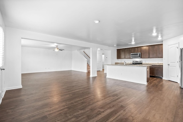 unfurnished living room featuring a ceiling fan, stairway, dark wood-style flooring, baseboards, and a sink