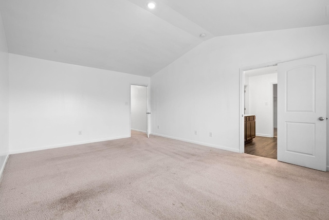 carpeted spare room featuring lofted ceiling and baseboards