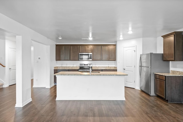 kitchen with appliances with stainless steel finishes, a sink, a kitchen island with sink, light stone countertops, and dark wood finished floors