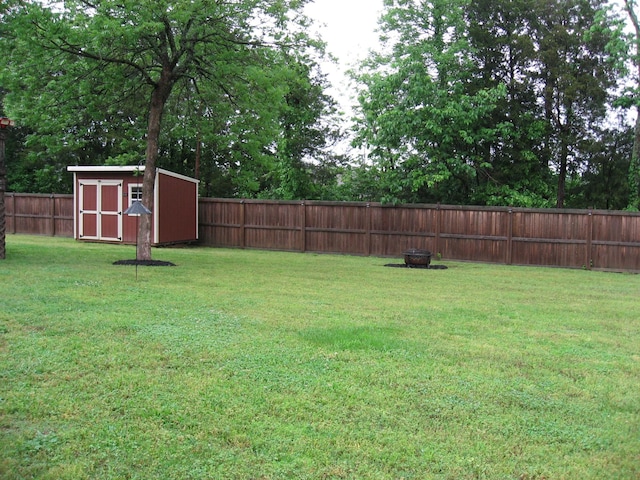 view of yard featuring an outbuilding, a fire pit, a storage shed, and a fenced backyard