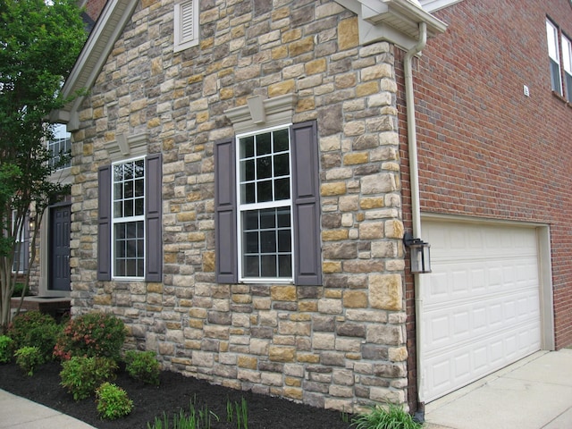 view of side of property featuring concrete driveway, brick siding, and stone siding