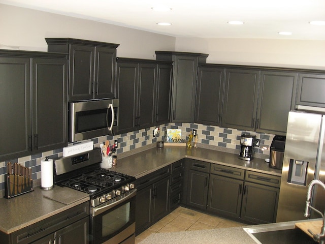 kitchen with a sink, backsplash, light tile patterned floors, and appliances with stainless steel finishes