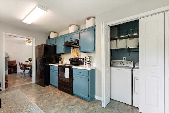 kitchen with washing machine and clothes dryer, blue cabinetry, decorative backsplash, under cabinet range hood, and black appliances