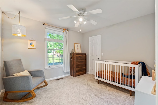 carpeted bedroom with baseboards, ceiling fan, a crib, and visible vents