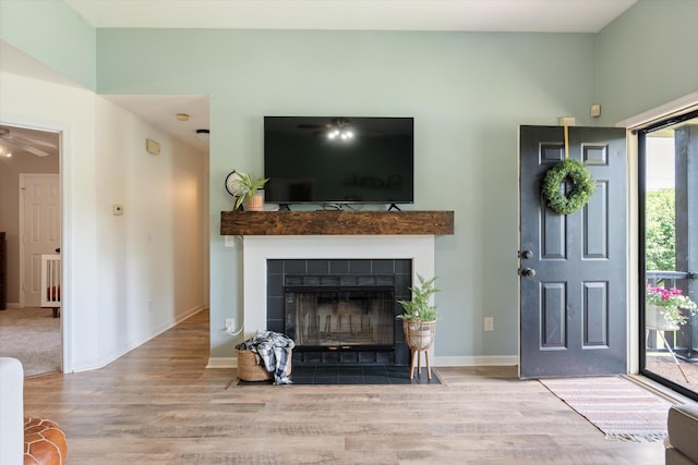 living area with a tiled fireplace, baseboards, ceiling fan, and wood finished floors