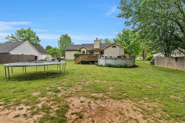view of yard featuring fence, a wooden deck, and a trampoline