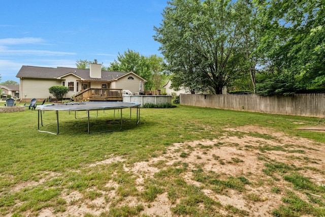 view of yard with a trampoline, fence, and a wooden deck