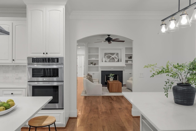 kitchen featuring arched walkways, ceiling fan, ornamental molding, and double oven