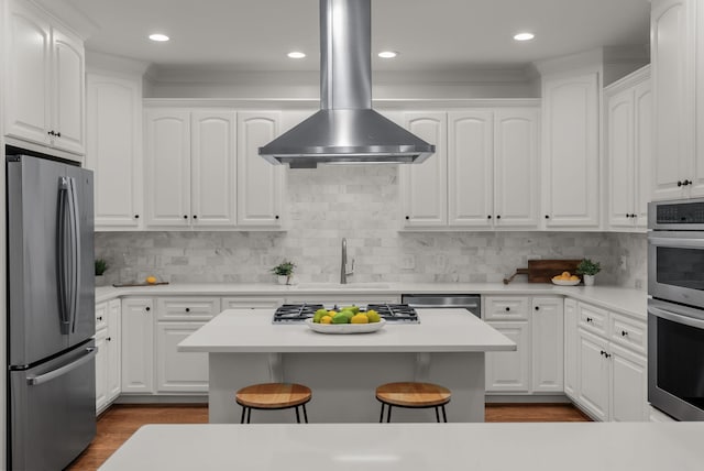 kitchen featuring a breakfast bar area, island exhaust hood, a sink, white cabinets, and stainless steel appliances