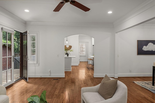 living area with arched walkways, ceiling fan, ornamental molding, and a healthy amount of sunlight