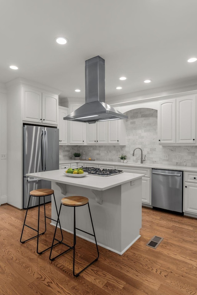 kitchen with white cabinets, stainless steel appliances, decorative backsplash, and island exhaust hood