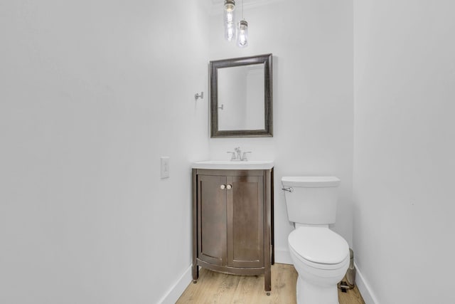 half bath with vanity, toilet, baseboards, and wood finished floors
