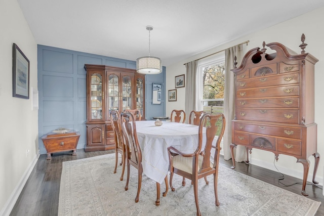 dining area with baseboards, a decorative wall, and wood finished floors