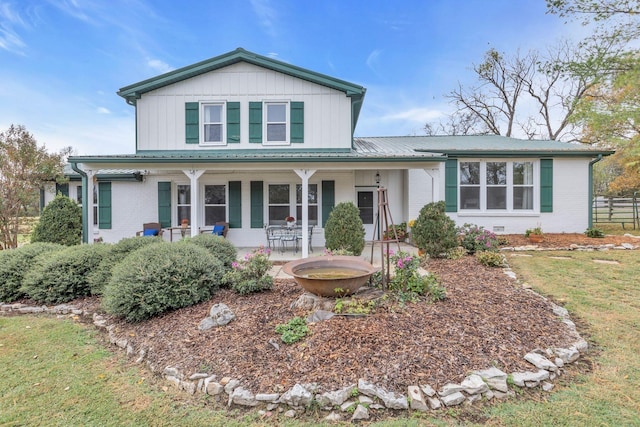 traditional home featuring covered porch, fence, brick siding, metal roof, and board and batten siding