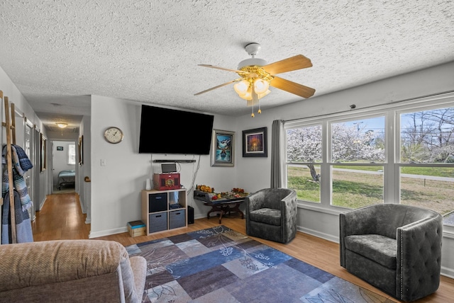 living room with a textured ceiling, wood finished floors, baseboards, and ceiling fan
