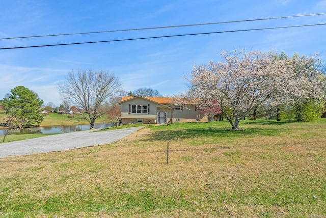 view of front of home featuring aphalt driveway, a water view, and a front yard