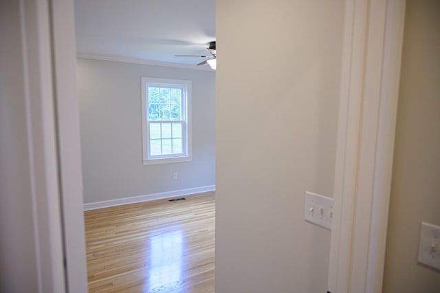 unfurnished room featuring a ceiling fan, baseboards, ornamental molding, visible vents, and light wood-type flooring
