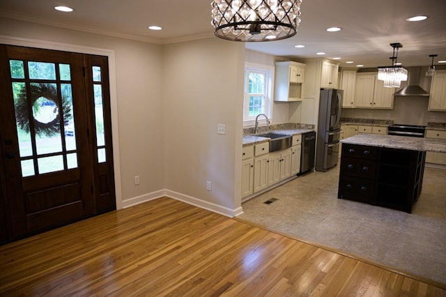 kitchen with a sink, wall chimney range hood, a chandelier, light wood-style flooring, and appliances with stainless steel finishes