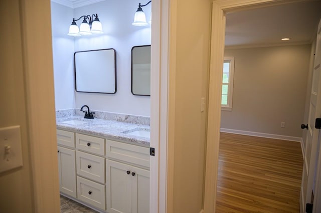 full bath featuring double vanity, wood finished floors, a sink, baseboards, and ornamental molding