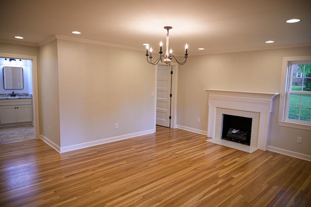 unfurnished living room with a sink, a notable chandelier, light wood-type flooring, ornamental molding, and recessed lighting