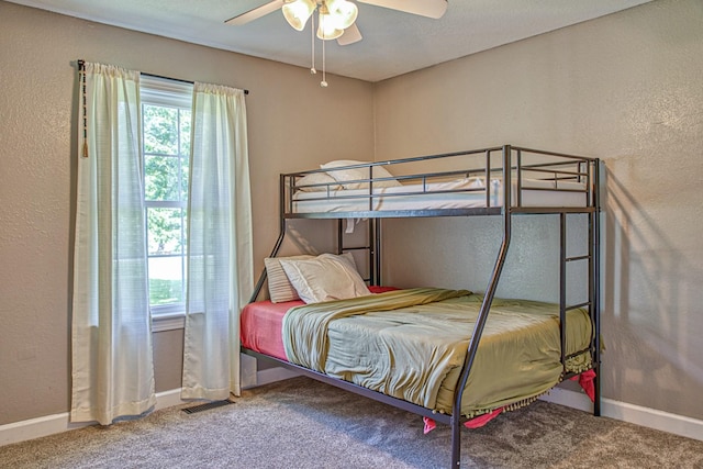 carpeted bedroom featuring ceiling fan, a textured wall, baseboards, and multiple windows